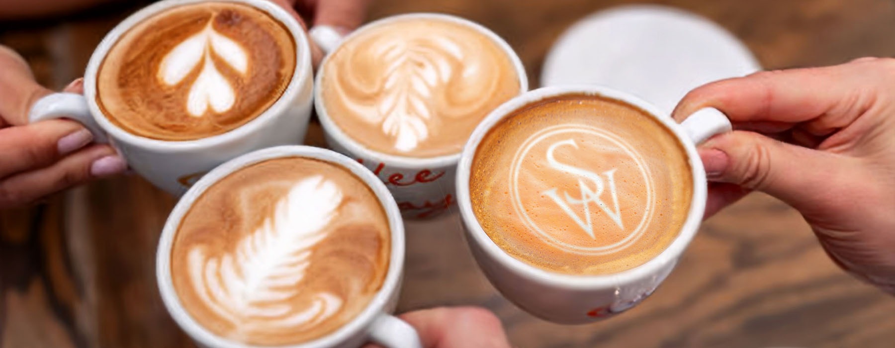 people hold cups of coffee together, showing off their foam designs
